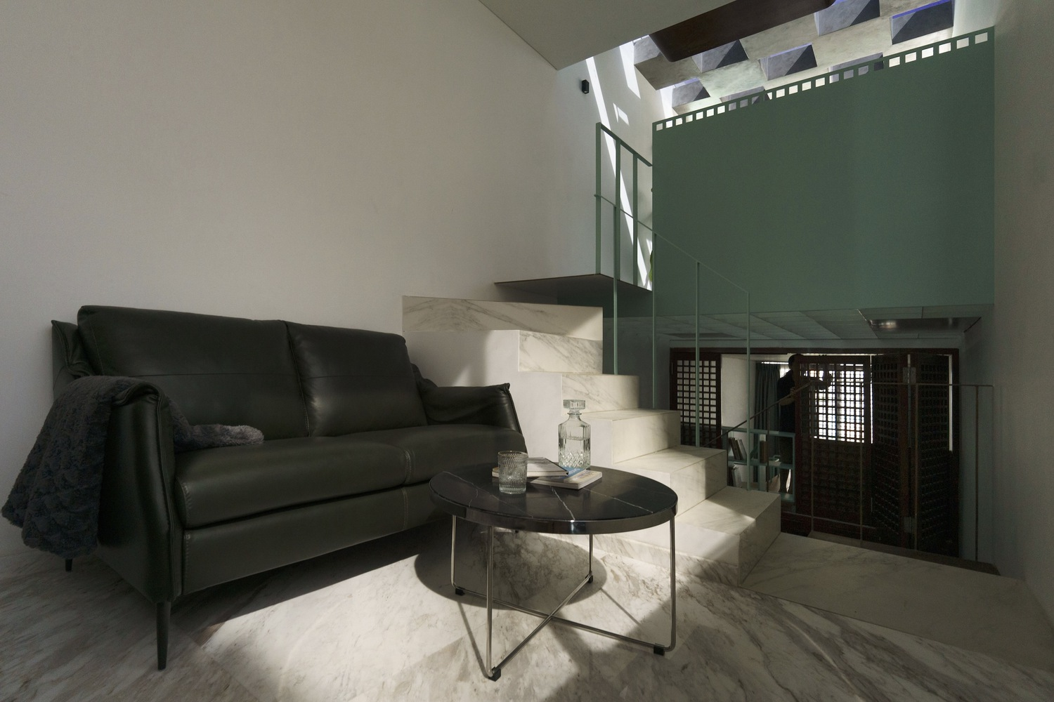 Sitting area with black leather sofa and marble clad stair illuminated by overhead skylight