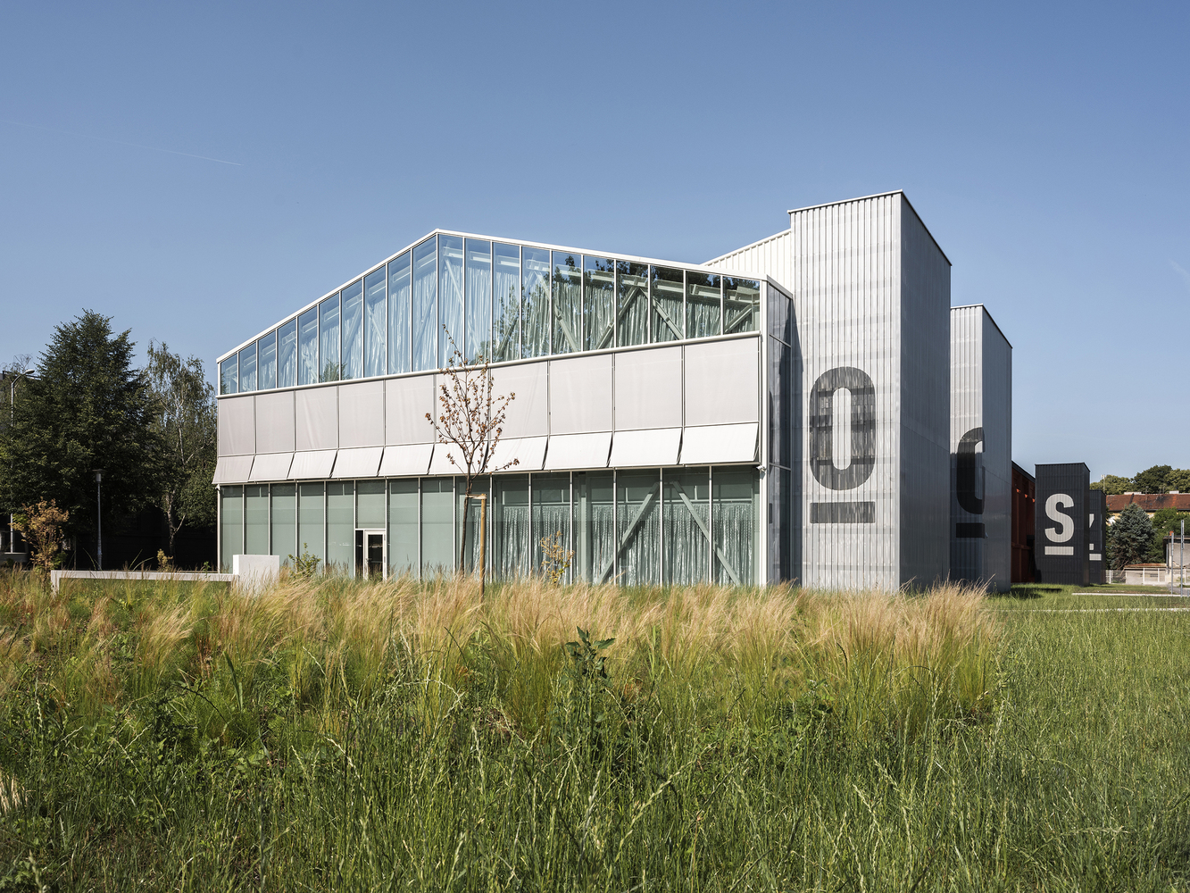 White panel and corrugated metal facade with glass clerestory level above ornamental grasses in late summer