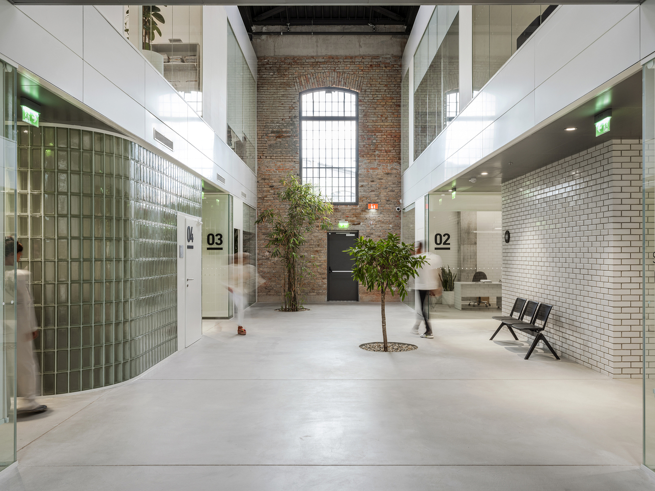Interior atrium with exposed brick wall and arched window flanked by white tile volumes and planted trees