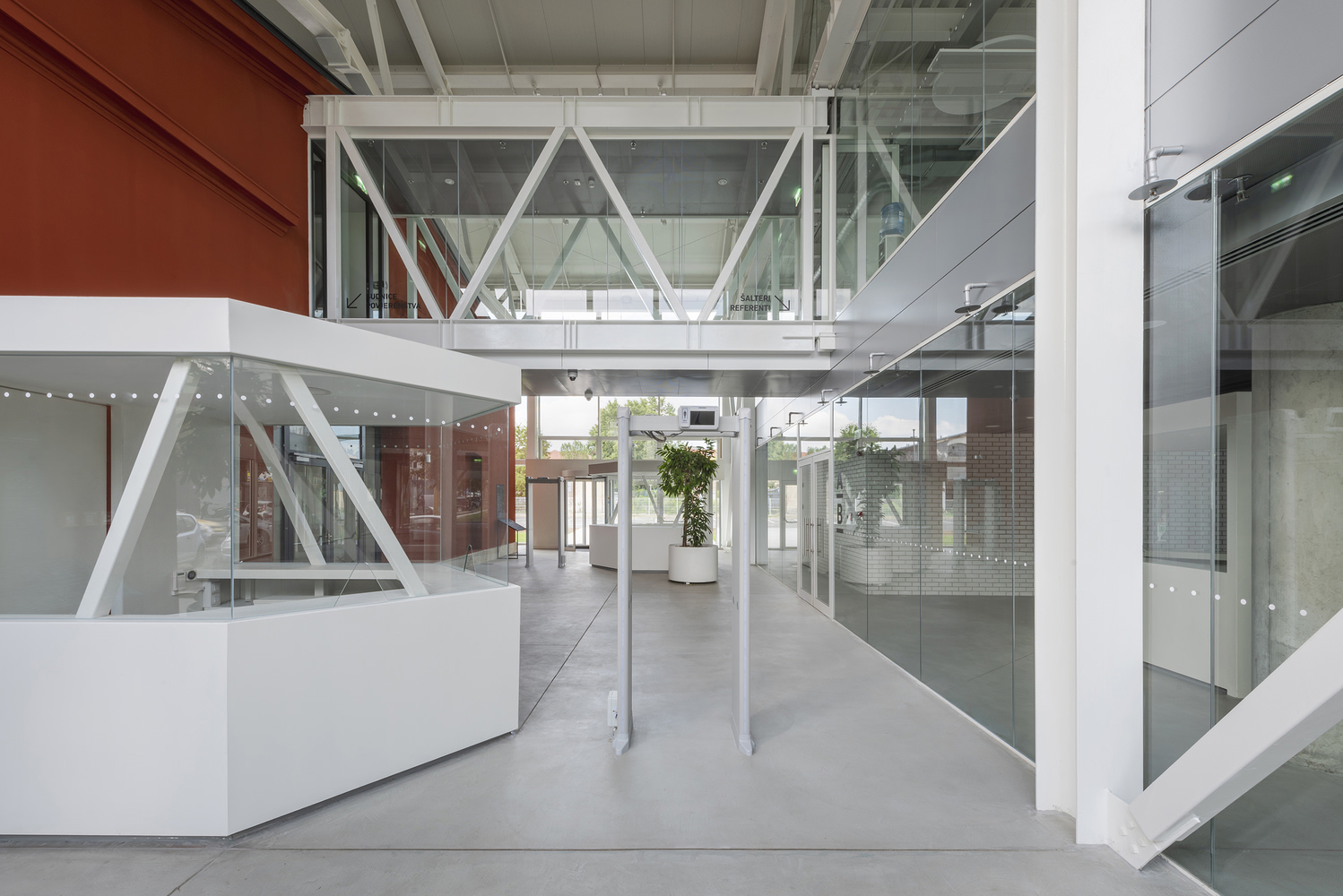 White steel bridge connecting upper levels across polished concrete entry hall with glass and metal facades