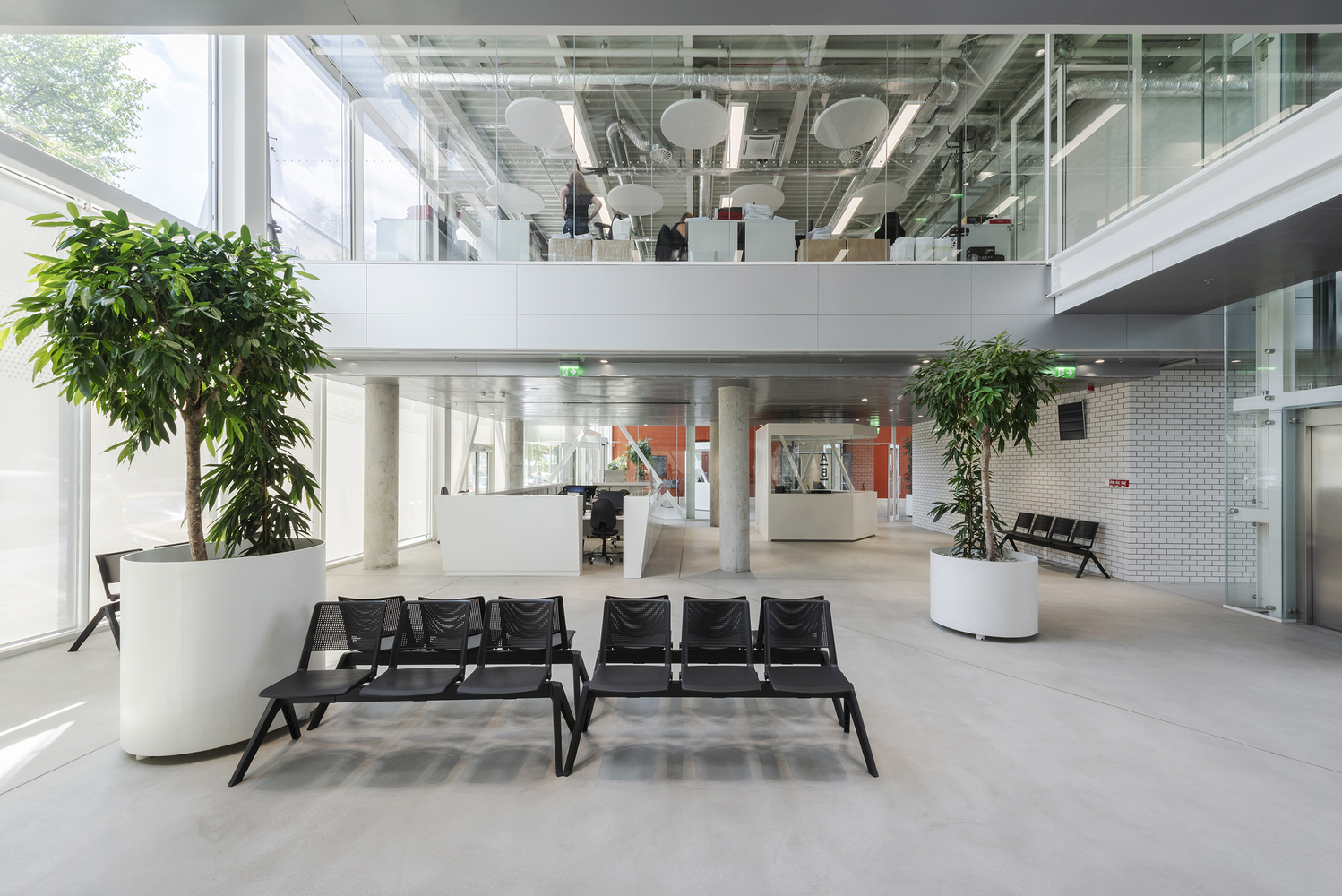Double-height atrium with exposed mezzanine, black lounge seating, and large planters in white pots