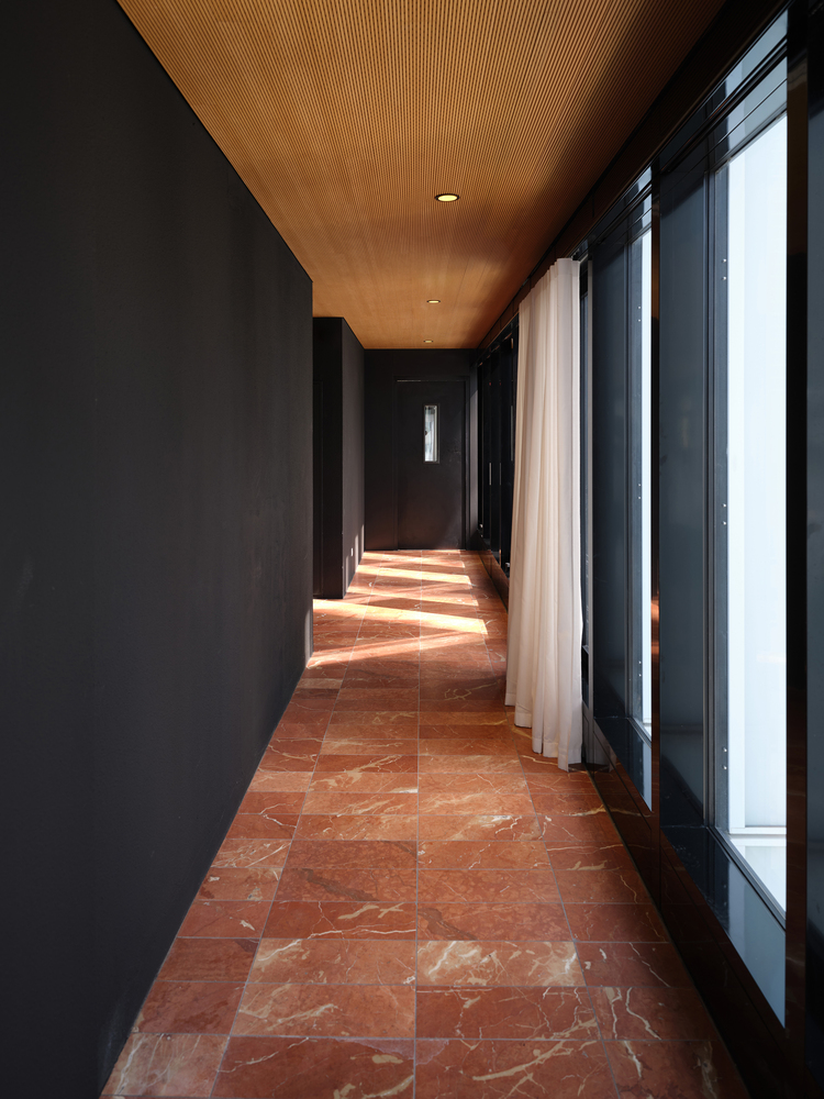 Corridor with red marble tile floor and timber slat ceiling casting afternoon shadows through glazed walls