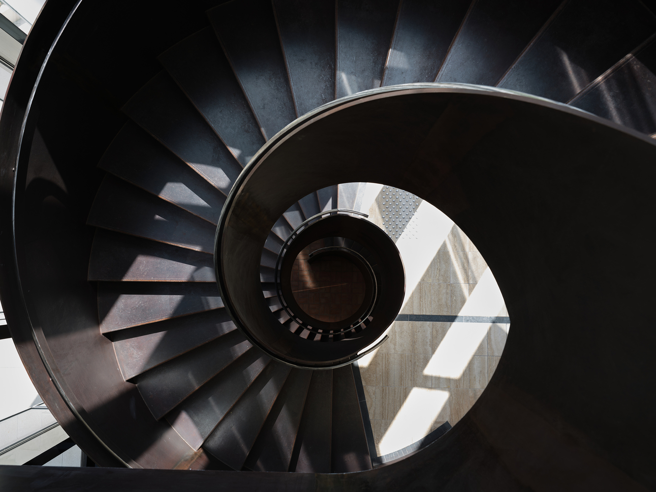 Top-down view of the spiral staircase with dark steel treads and sunlight illuminating the central void