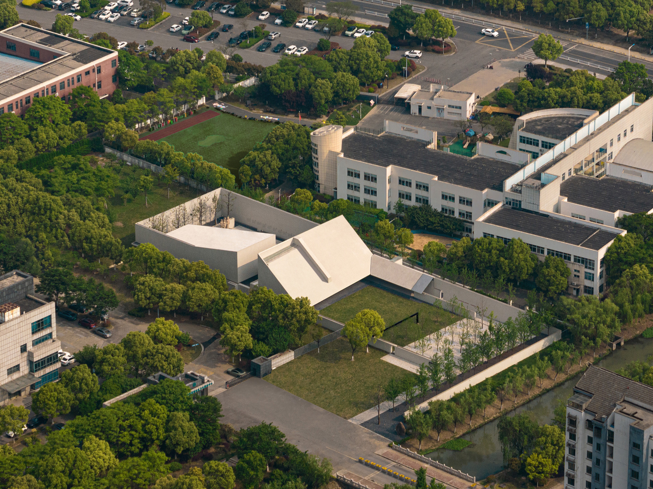 Aerial view of white folded roof volumes set within a campus courtyard surrounded by trees