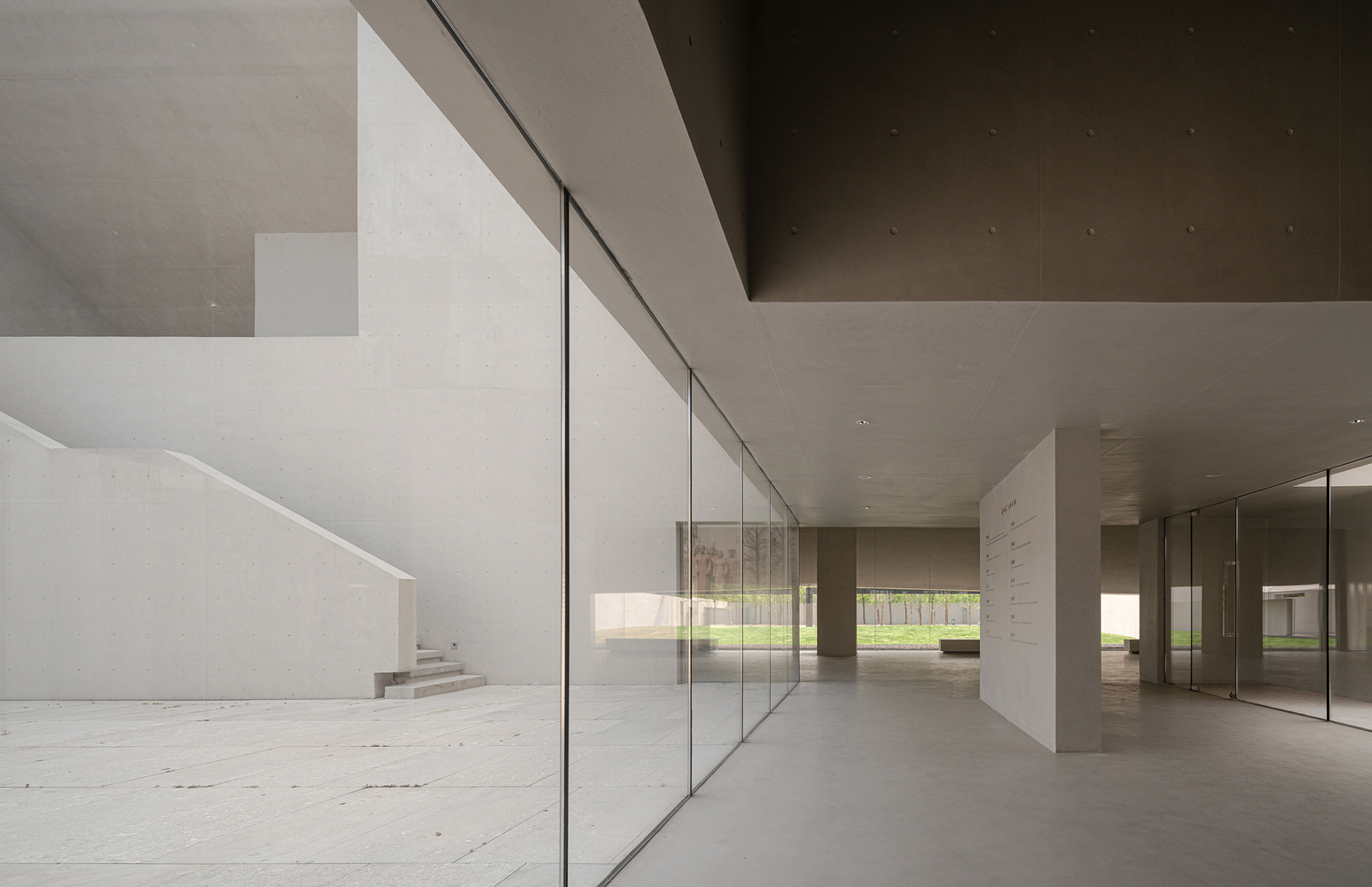 Interior corridor with full-height glass wall, concrete ceiling and glimpse of staircase at left