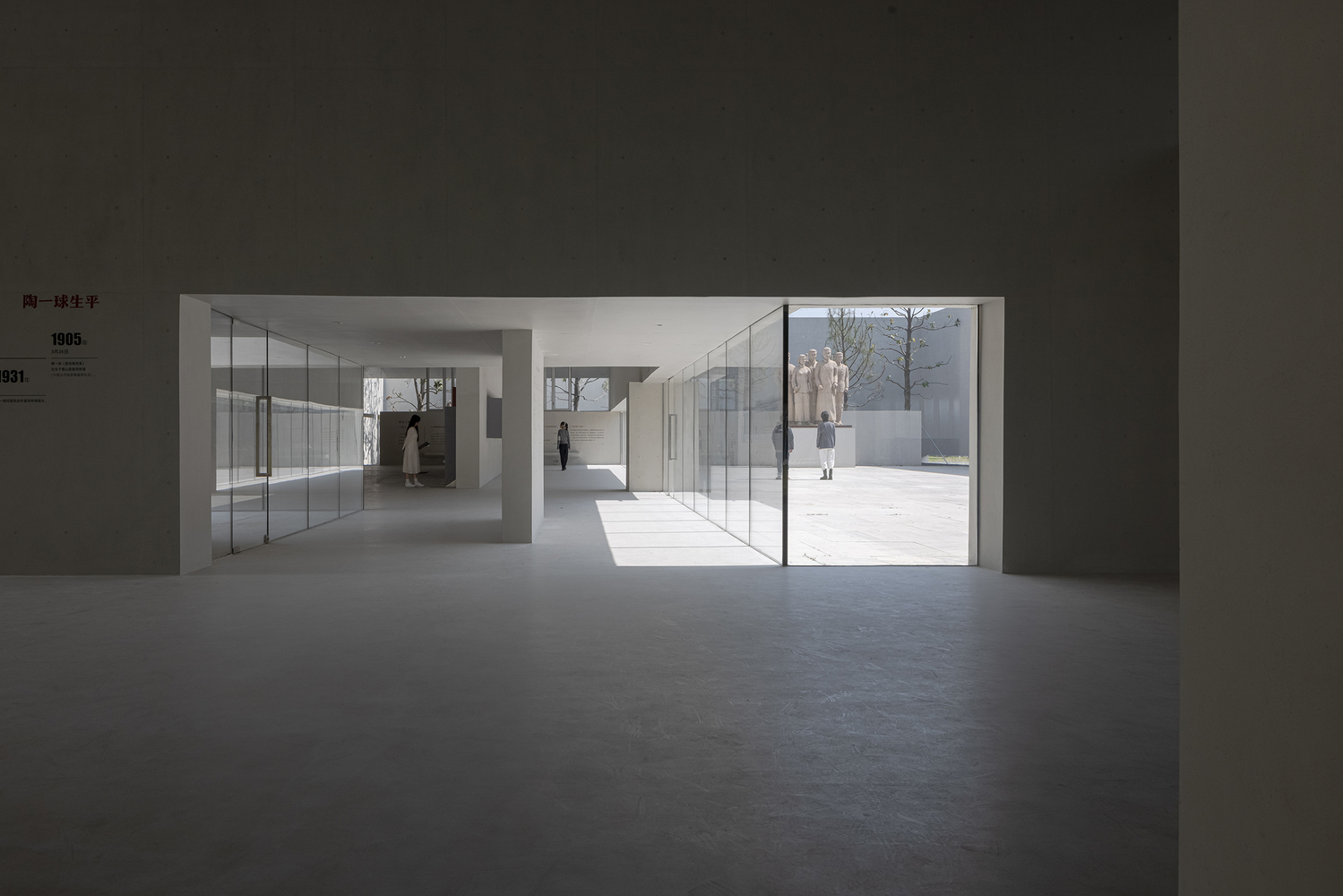 Gallery space looking through glass doors toward exterior courtyard with visitors walking in sunlight