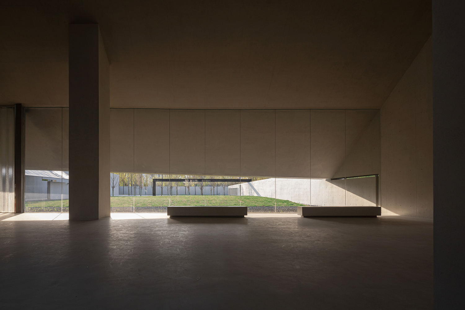 Exhibition hall with low benches and a horizontal window framing a view of the landscape outside