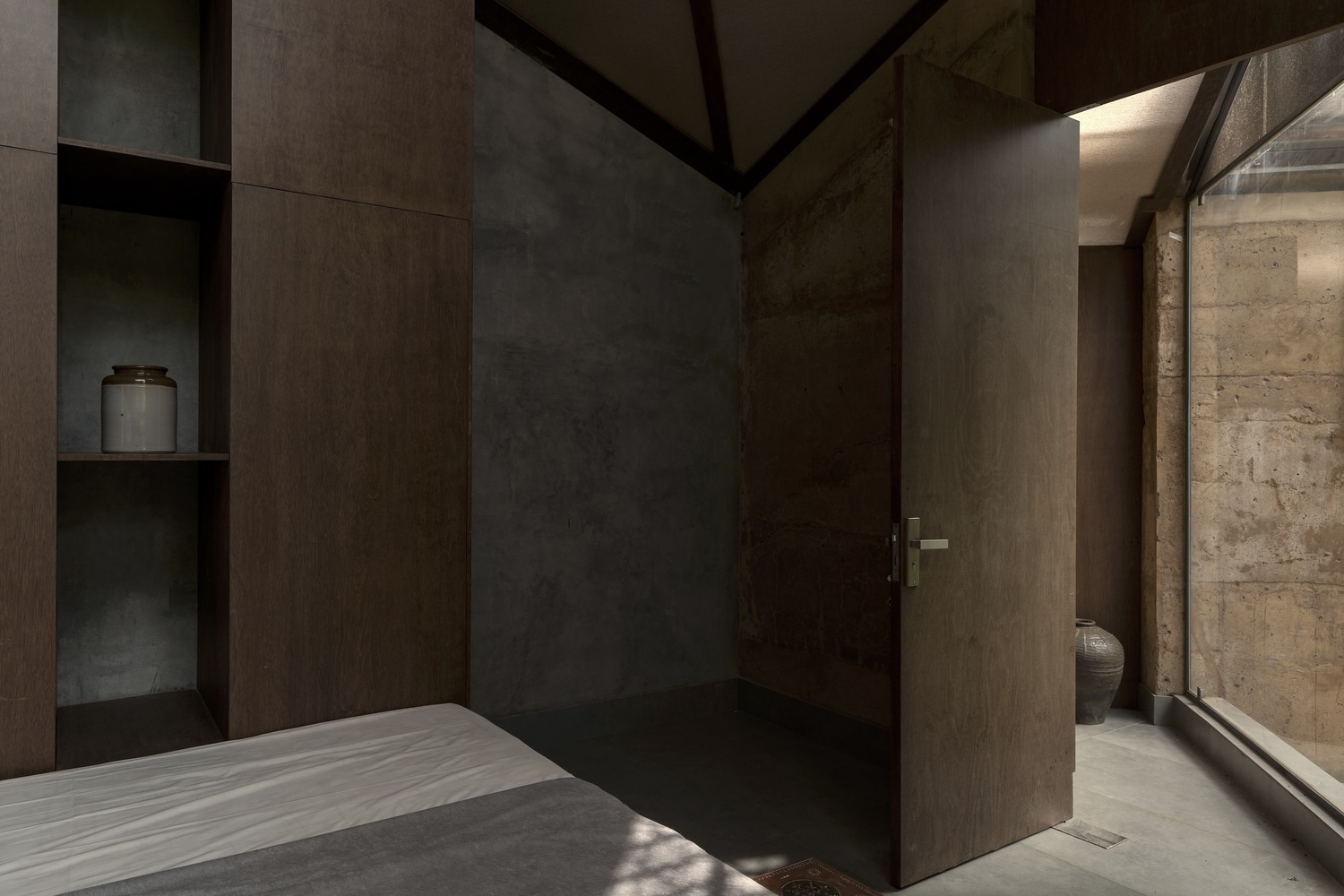 Interior room with dark timber panels, built-in niches, and a pivoting door opening to a concrete corridor