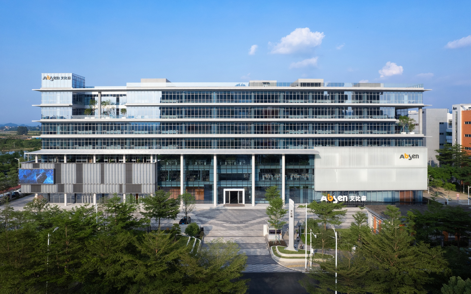 Front elevation showing the cantilevered floor slabs and landscaped approach plaza under afternoon sun