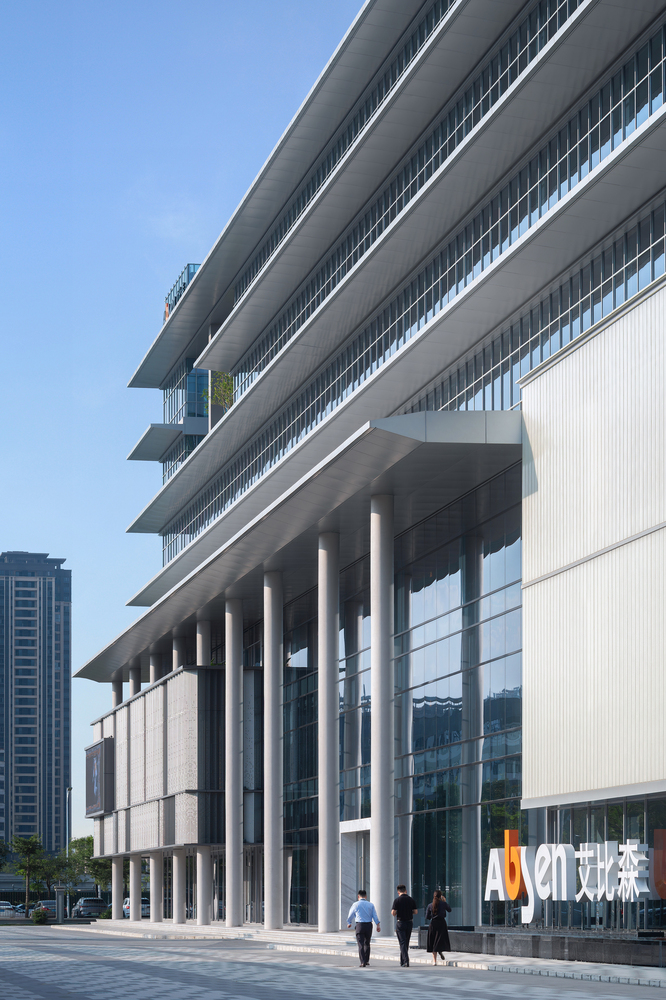 Corner detail of the overhanging floor plates supported by white cylindrical columns with pedestrians below