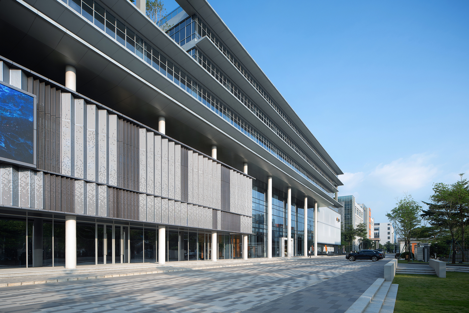 Side facade with ribbed concrete panels between cylindrical columns and a paved street alongside