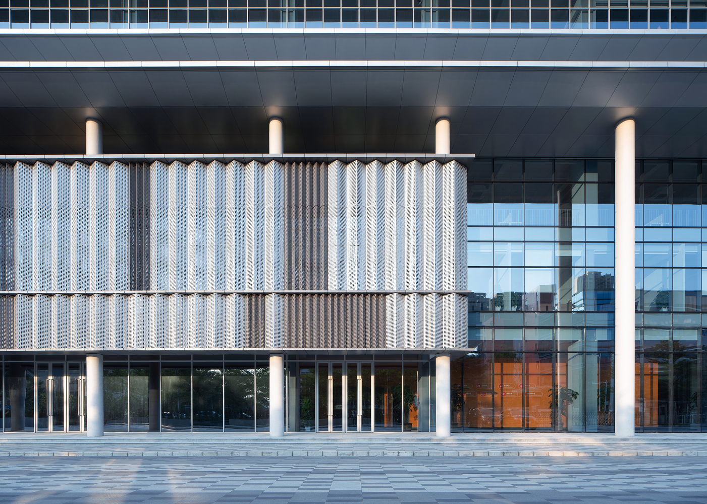 Close view of the corrugated precast panel wall with cylindrical columns and glazed entrance behind