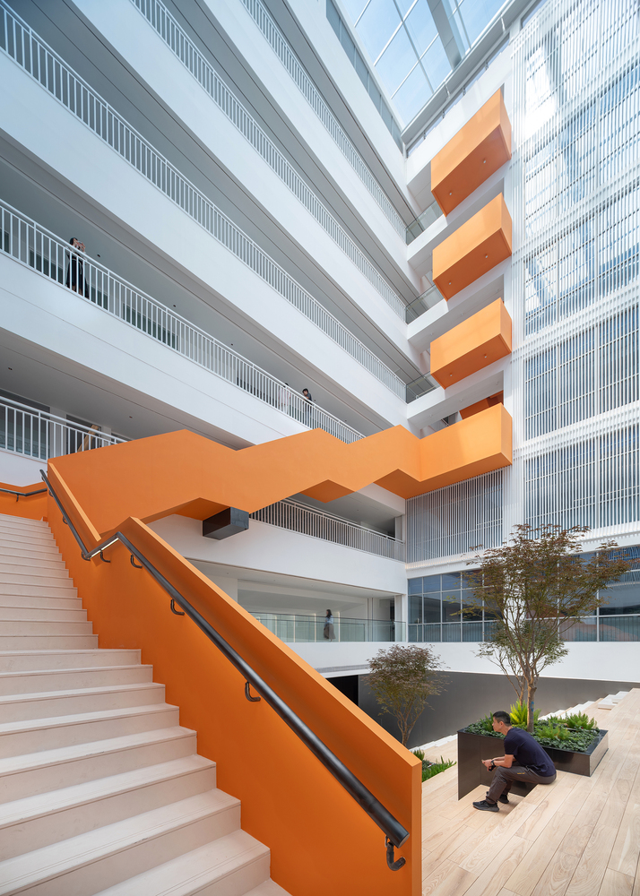 Orange zigzag staircase descending into a courtyard with planted trees and a person crouching near a planter