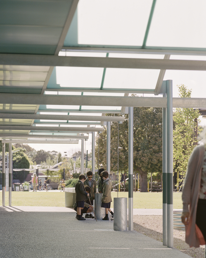Covered walkway with steel beams and glazed roof panels sheltering children in school uniforms