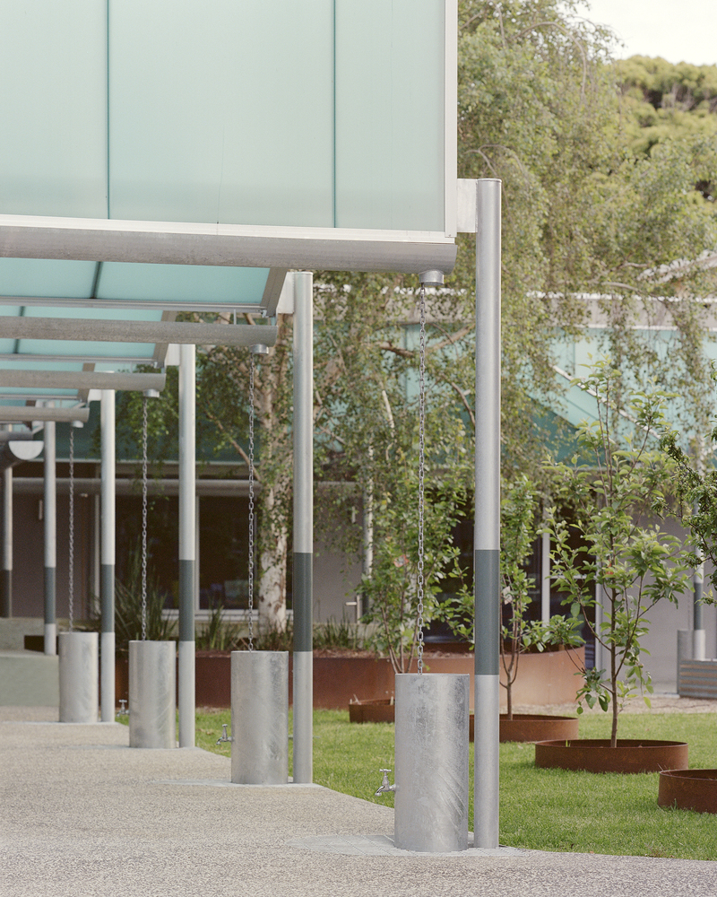 Detail of cylindrical steel columns and horizontal beams beside young trees in concrete planters
