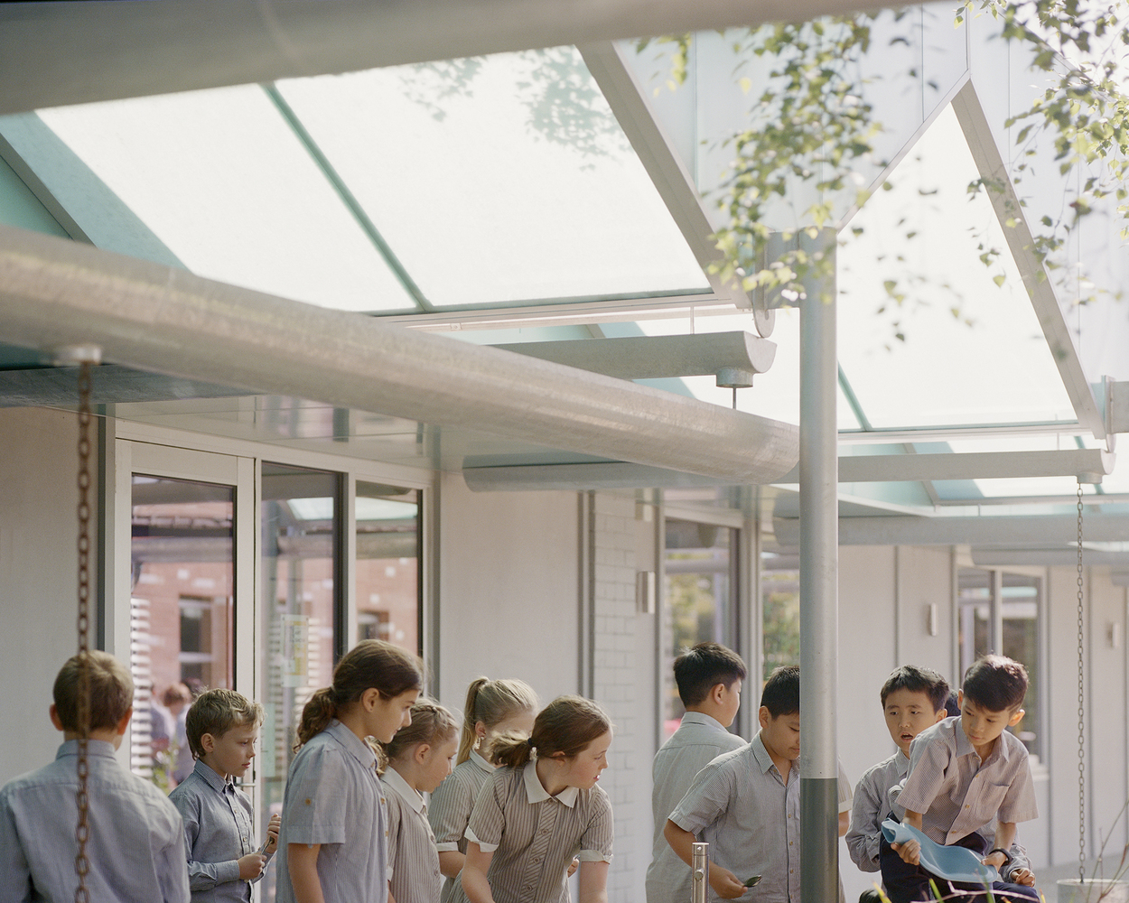 Students gathered under the translucent canopy with exposed steel structure and glazed panels overhead