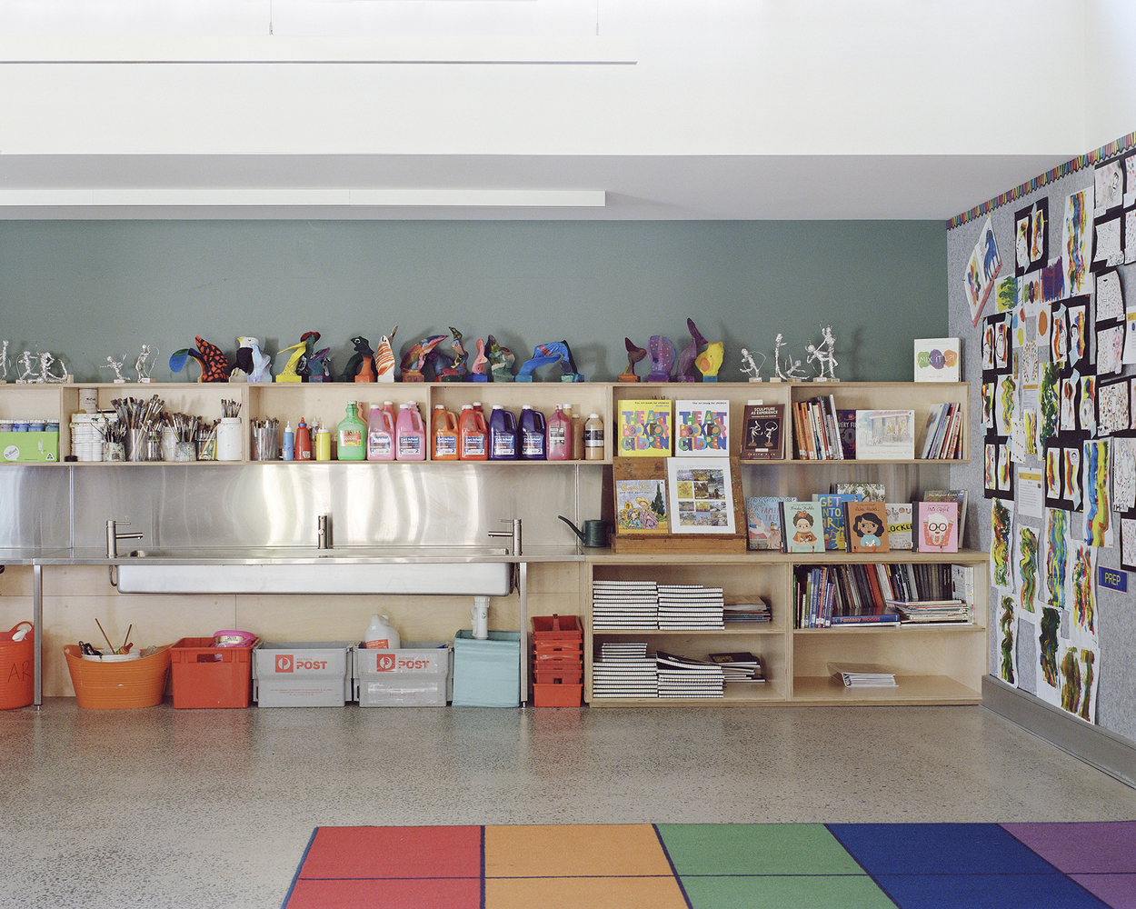 Classroom storage wall with plywood shelving, dual sinks, art supplies and children's work pinned above