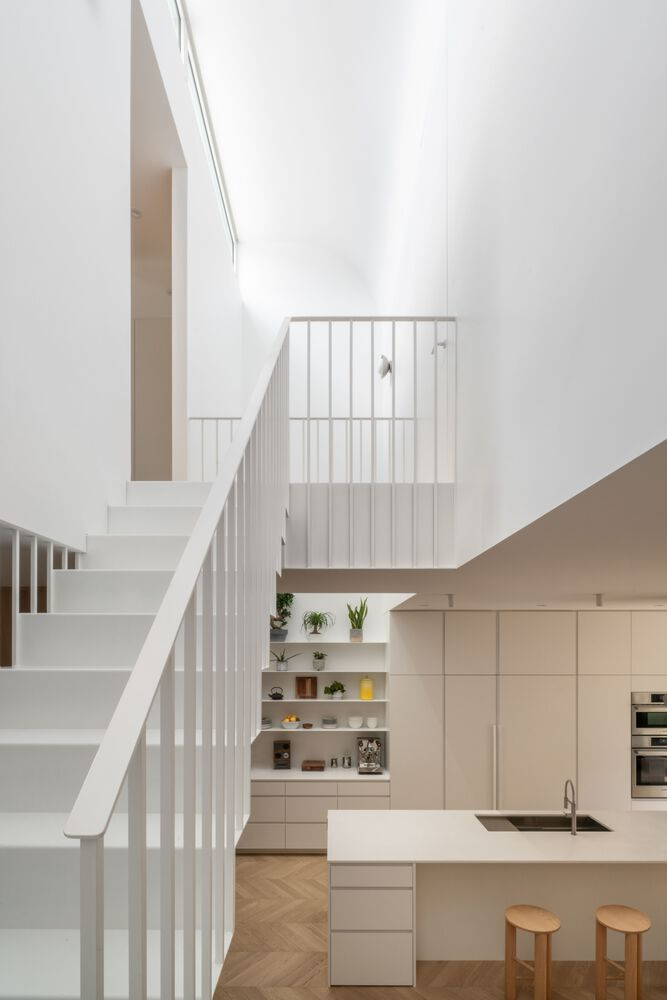 White-painted staircase with vertical balusters rising past the kitchen island and open shelving