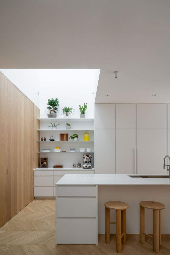 Kitchen island with white countertop and timber stools beneath a rectangular skylight with potted plants