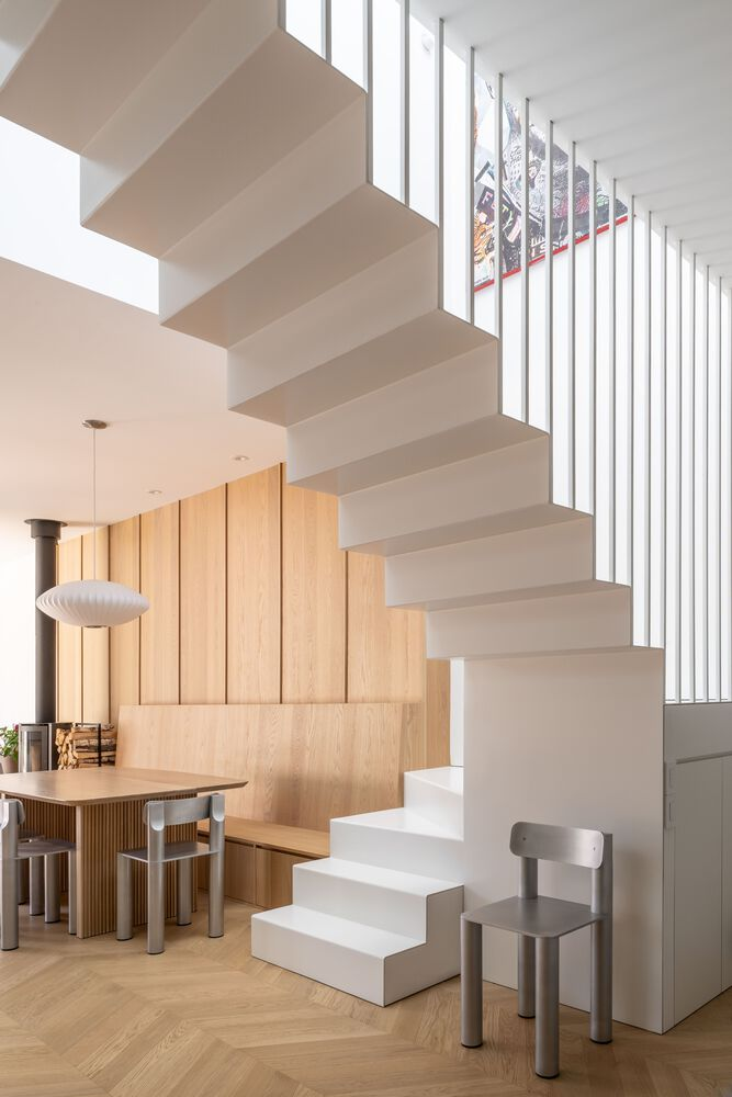 Floating white staircase with vertical slat balustrade filtering natural light from a clerestory window