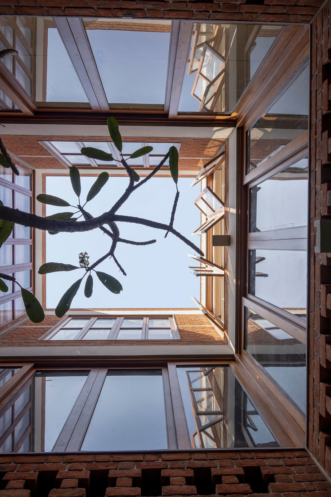 Looking up through the open courtyard with timber-framed balconies and a plumeria tree overhead