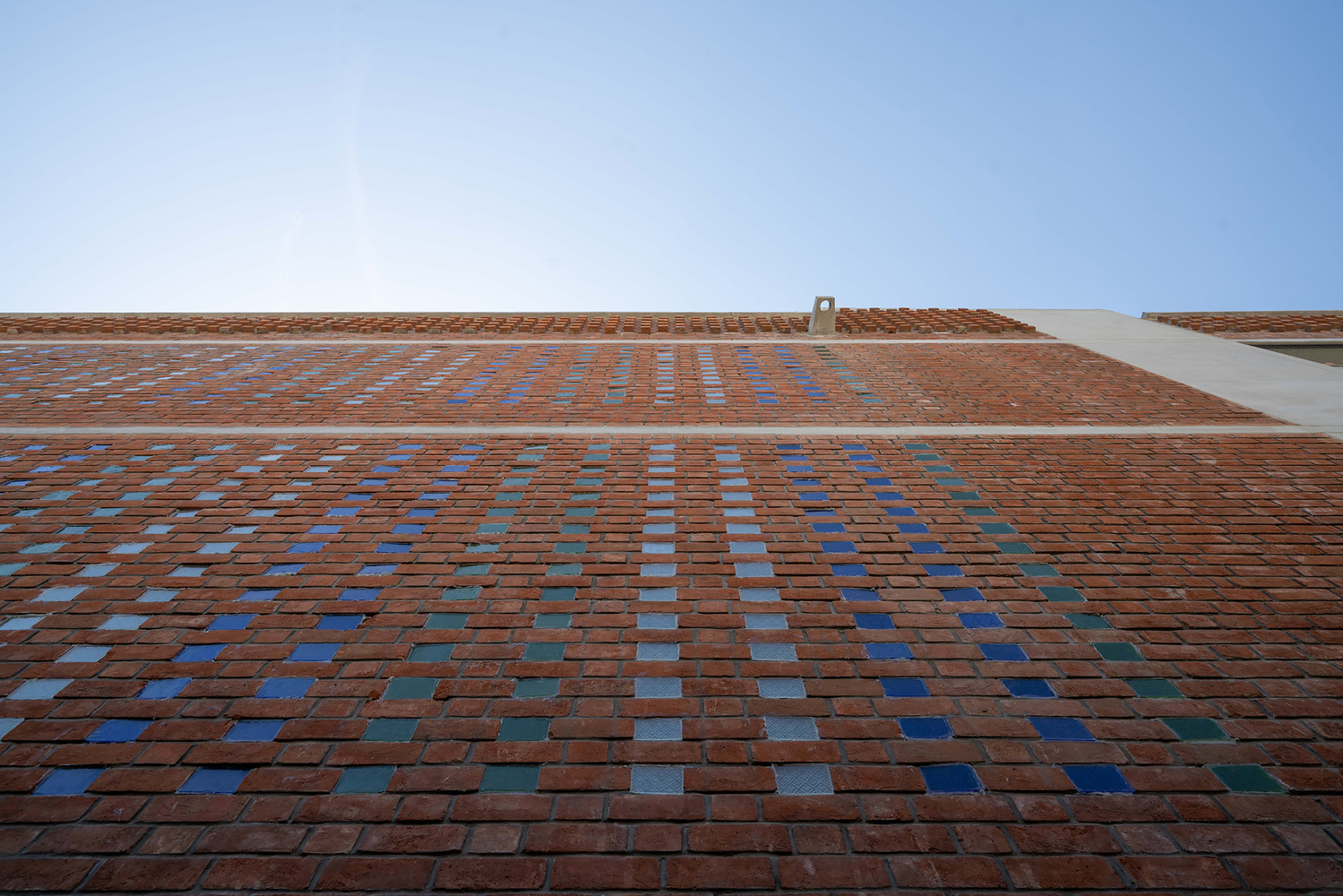 Upward view of brick facade with scattered blue tile accents under clear sky