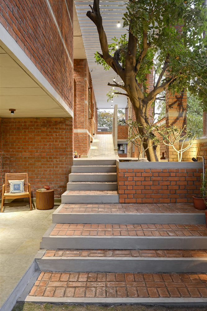 Outdoor staircase with brick treads and concrete risers ascending past a preserved tree in the courtyard