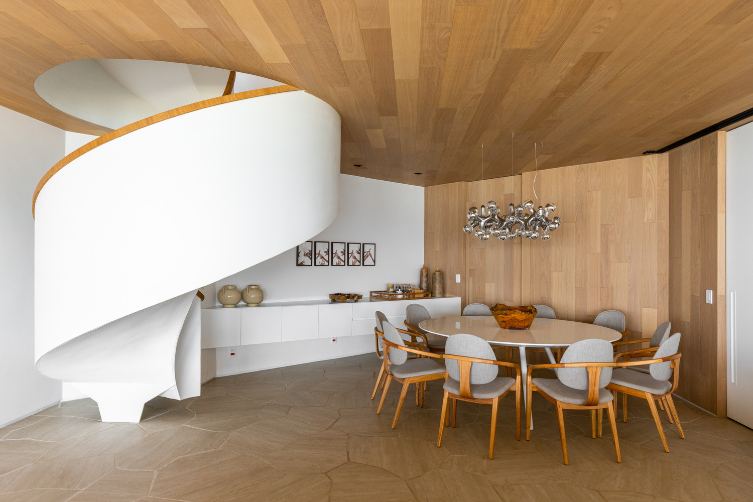 Dining area with sculptural white staircase and radiating timber ceiling panels