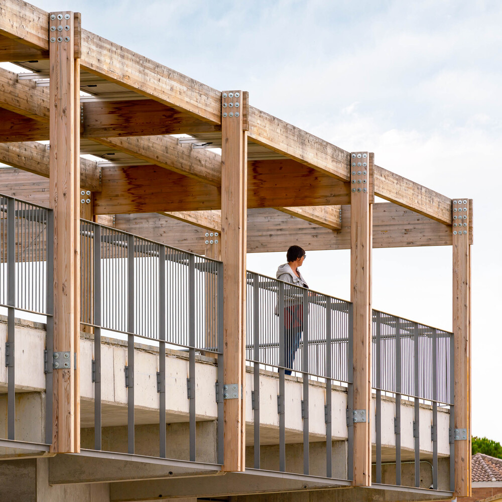 Timber posts and beams with metal brackets supporting the canopy above a person on the walkway