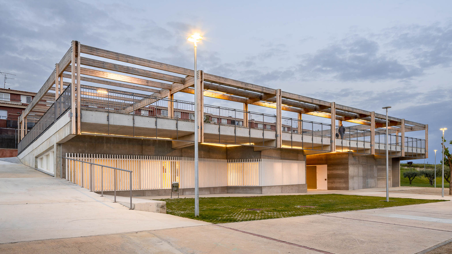 Exterior corner of the pavilion with exposed timber roof structure and warm interior lighting at dusk