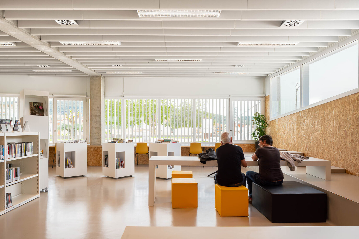 Interior library space with oriented strand board panels, orange seating cubes and suspended white ceiling baffles