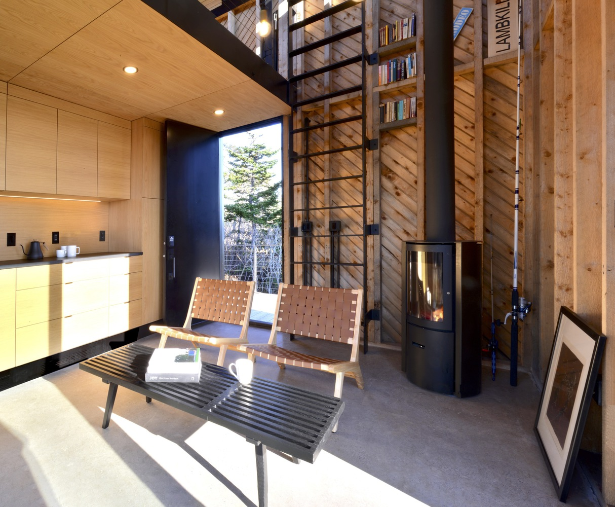 Steel ladder leading to a mezzanine library beside a cylindrical wood stove and chevron timber wall