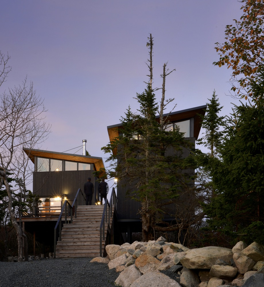 Timber stair bridge connecting two pavilions over a rocky outcrop as visitors ascend at twilight