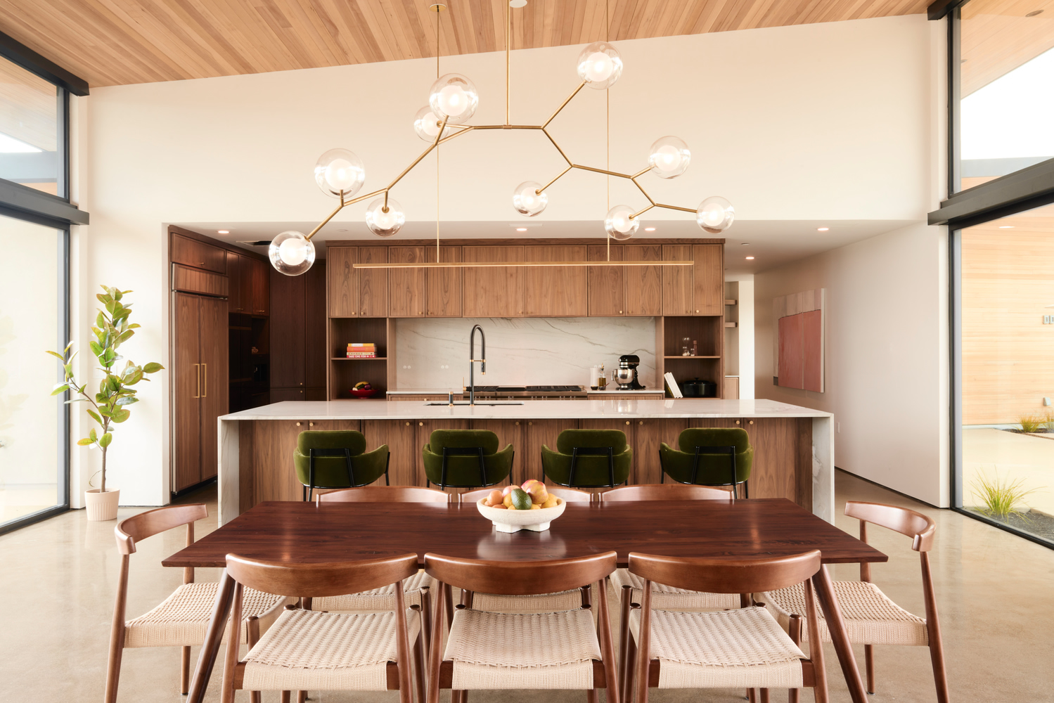 Open kitchen with walnut cabinetry and island featuring green velvet stools beneath a timber ceiling