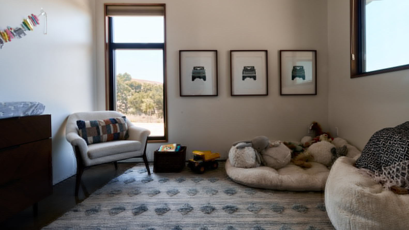 Bedroom with timber-framed window overlooking a hillside and three framed prints above a floor cushion