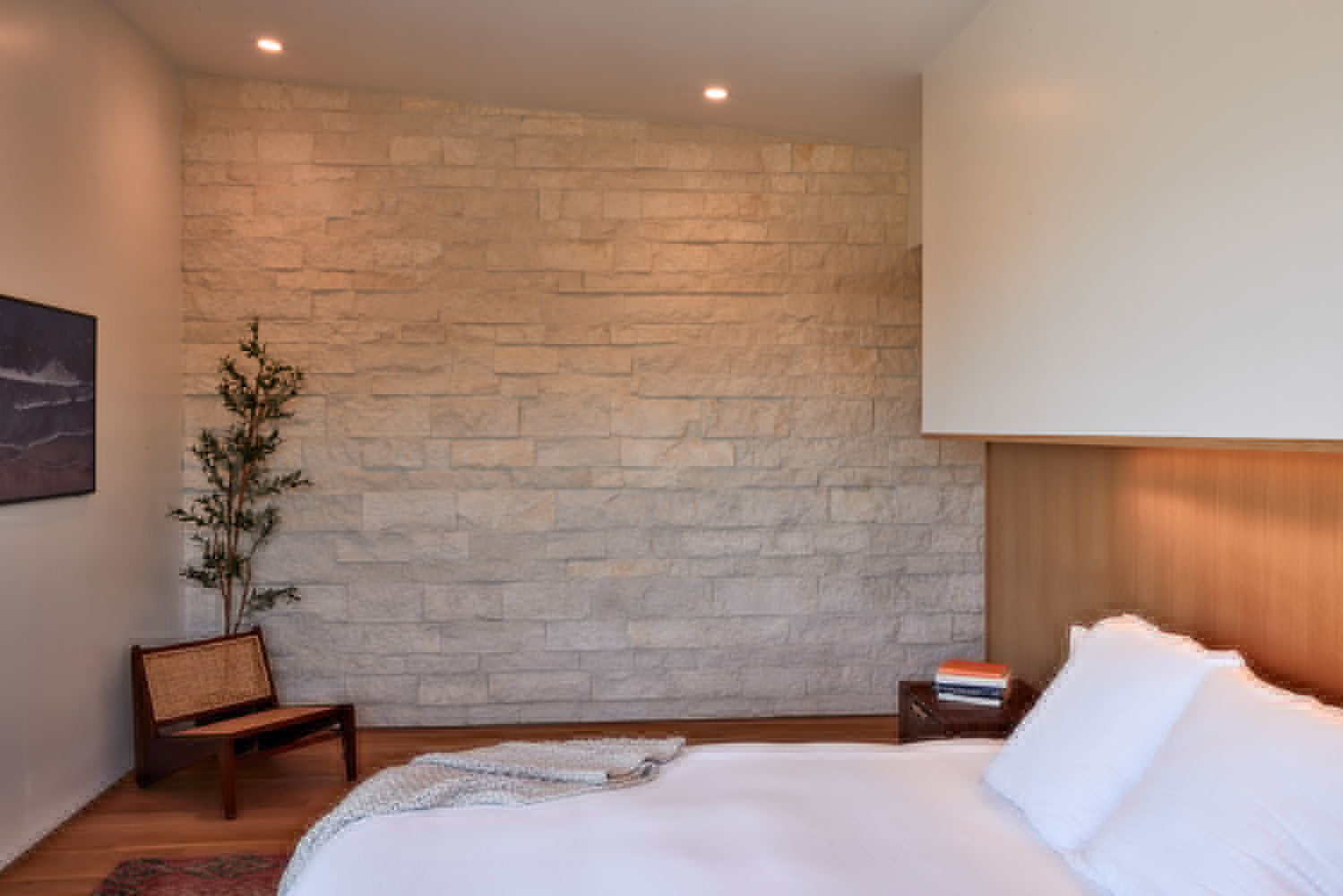 Bedroom with limestone ledge-stone accent wall and small potted tree beside the bed