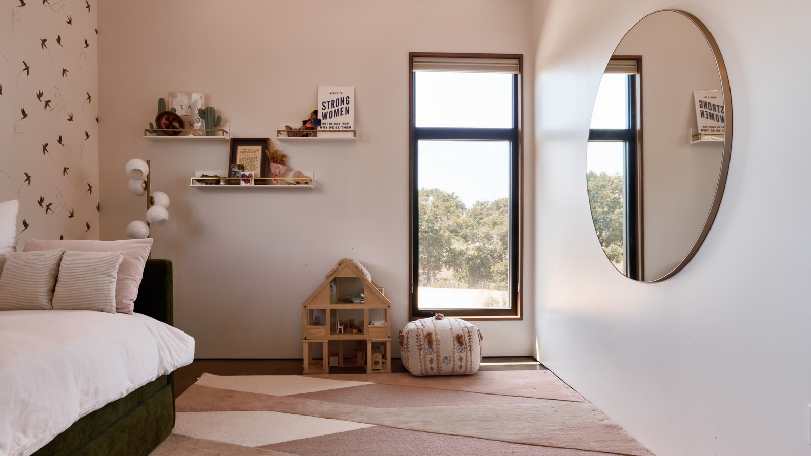 Bedroom with oval brass mirror and vertical windows overlooking treetops in soft daylight