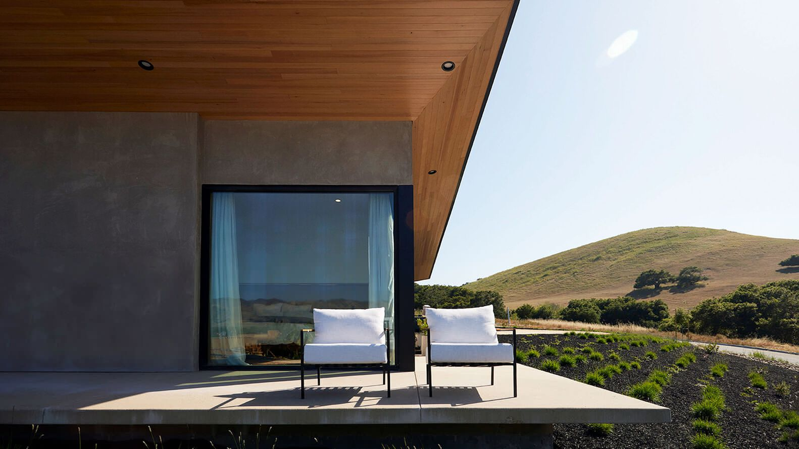 Covered terrace with timber soffit and two white chairs facing rolling hills in afternoon sun