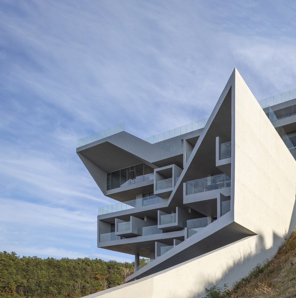 Angled view of cantilevered concrete floors and glass balustrades against a wooded hillside