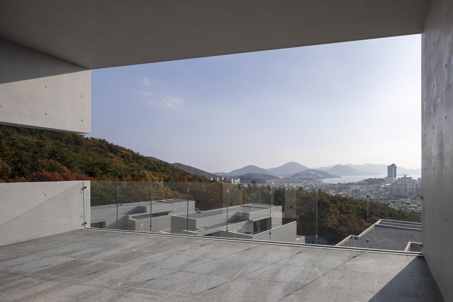 Rooftop terrace with glass railing overlooking coastal mountains and distant harbor
