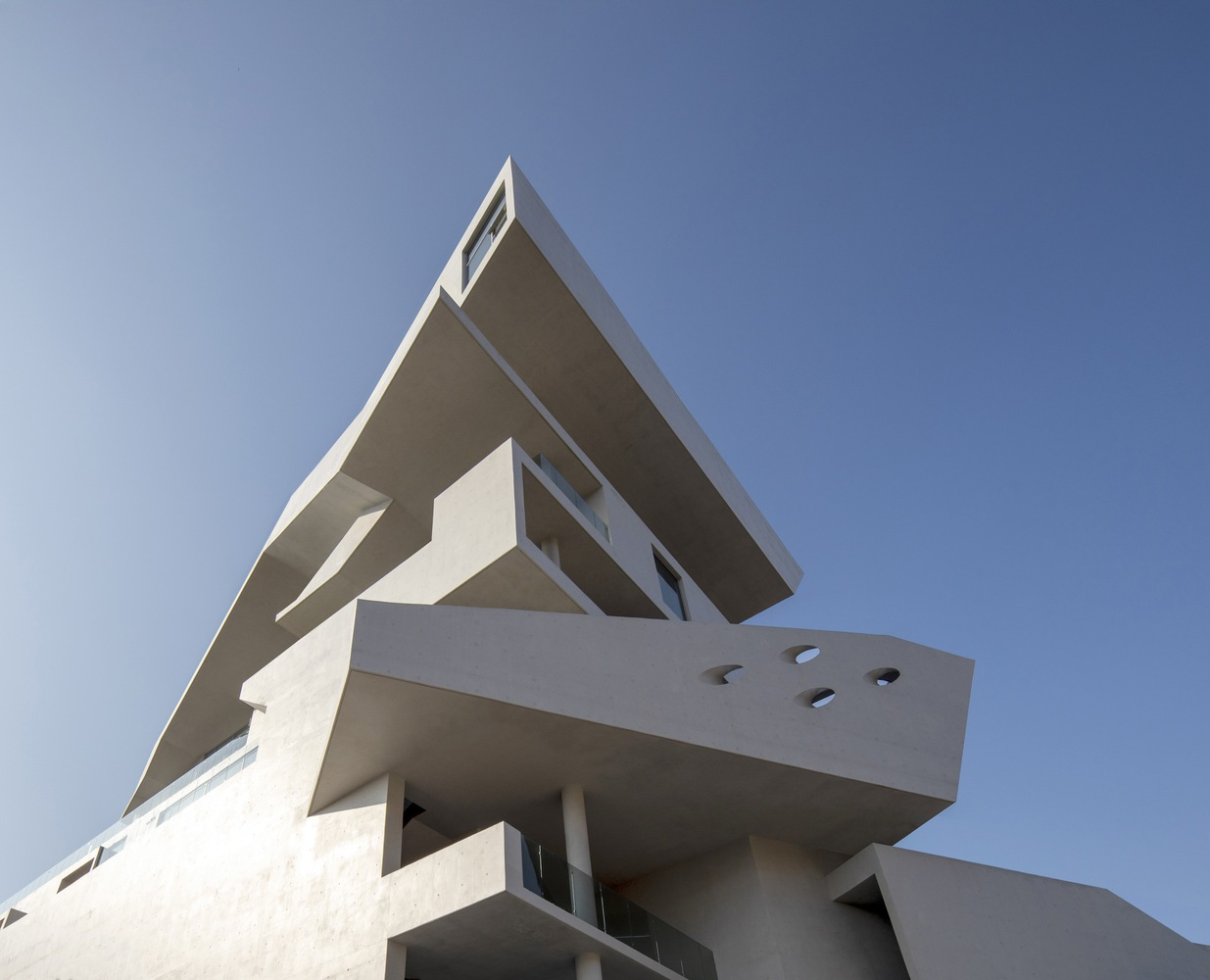 Upward view of cantilevered concrete slabs with circular perforations under clear blue sky
