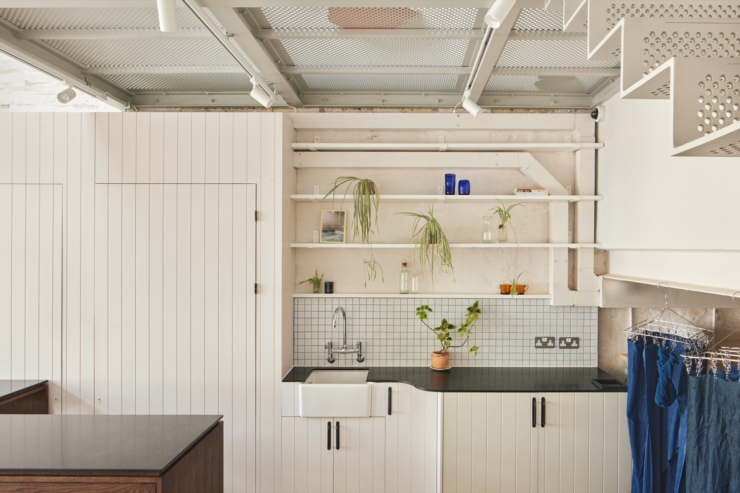 Kitchen counter with white tile backsplash and open timber shelves holding potted plants
