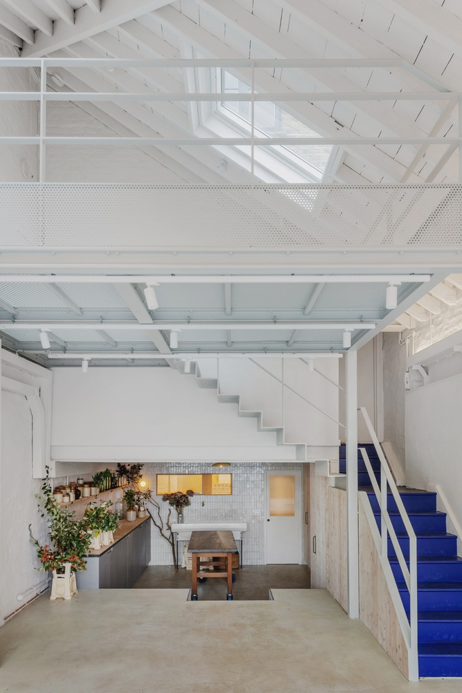 Double-height space showing mezzanine with perforated metal panels and blue staircase below
