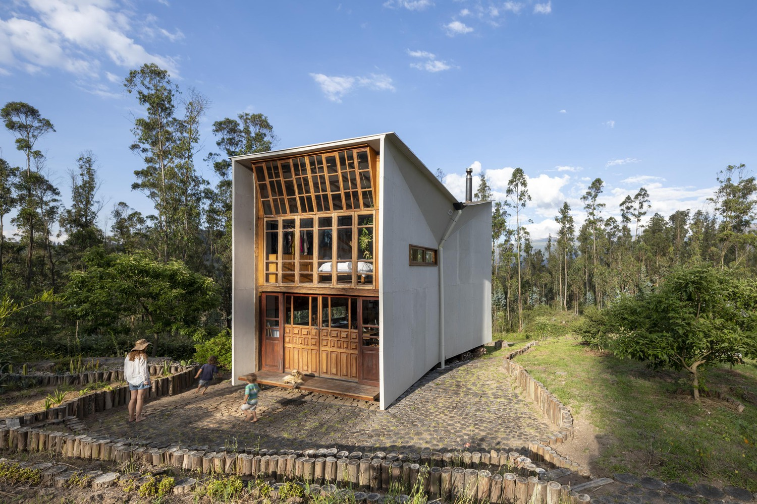 Front facade view with glazed timber grid and white angled walls as a figure stands near the entrance path