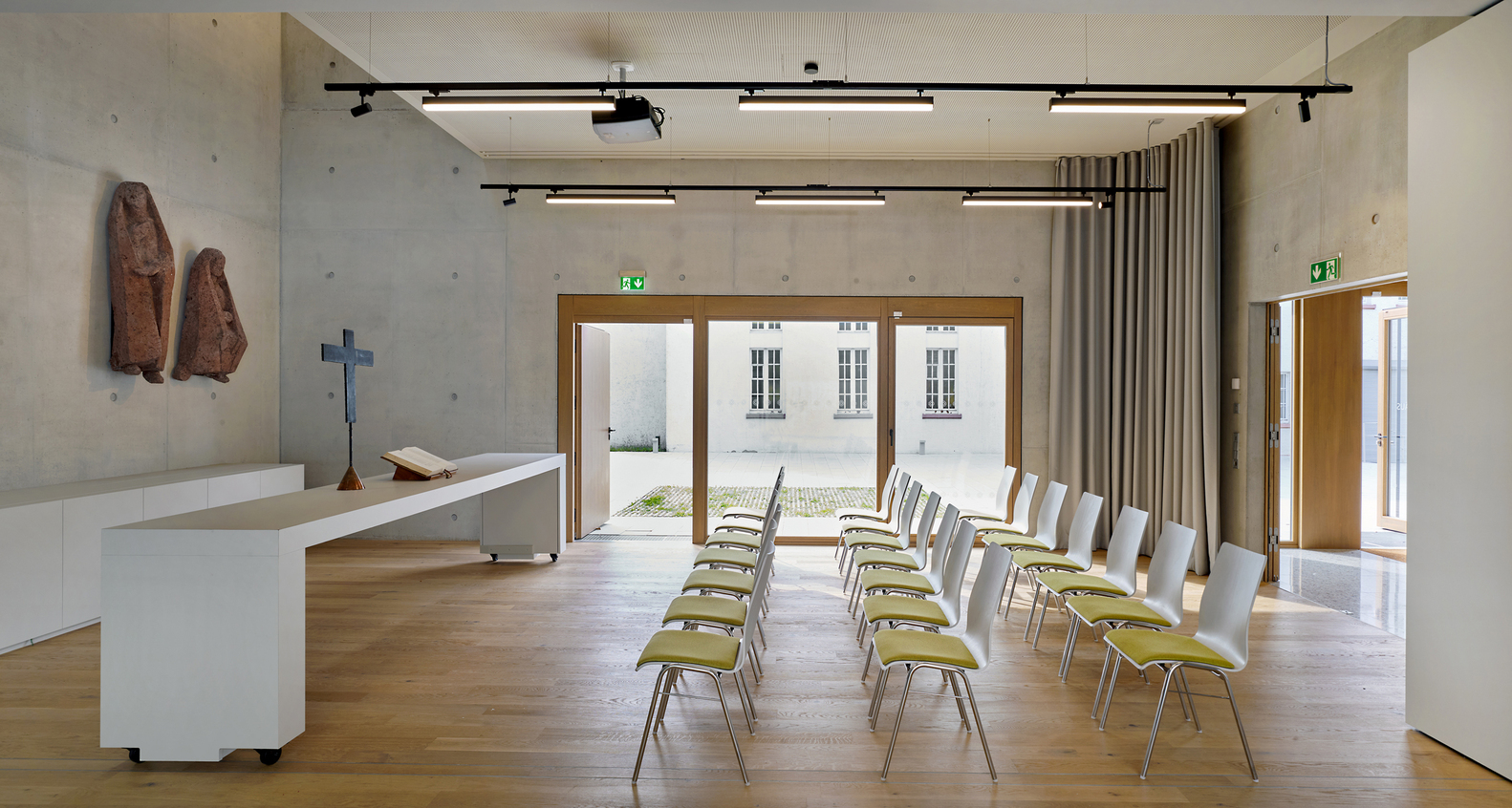 Chapel interior with white altar, rows of seating facing glazed doors opening to a paved courtyard