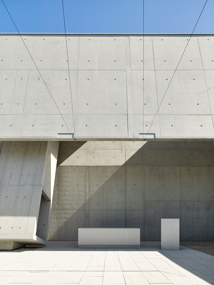 Exterior courtyard corner showing white altar and lectern against board-formed concrete walls under clear sky