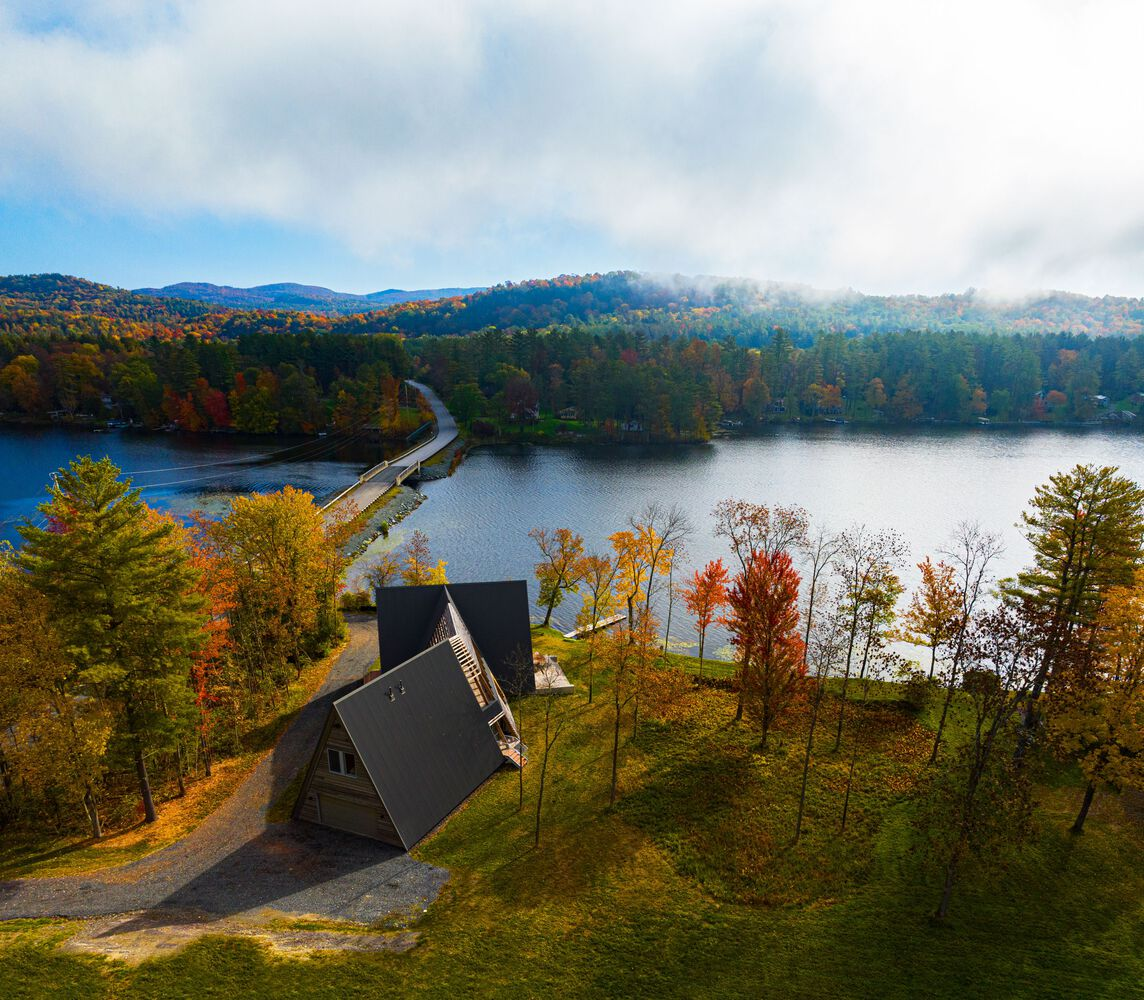 Aerial view of the A-frame structure on a sloped lakeside site with fall foliage and morning mist