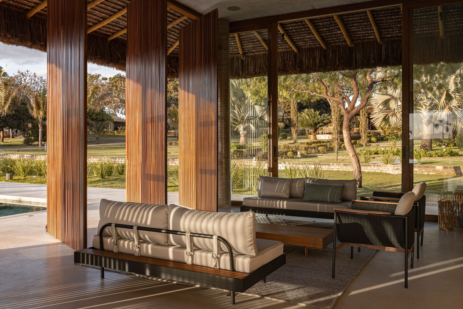 Covered lounge area with vertical timber screens filtering afternoon light from the planted exterior