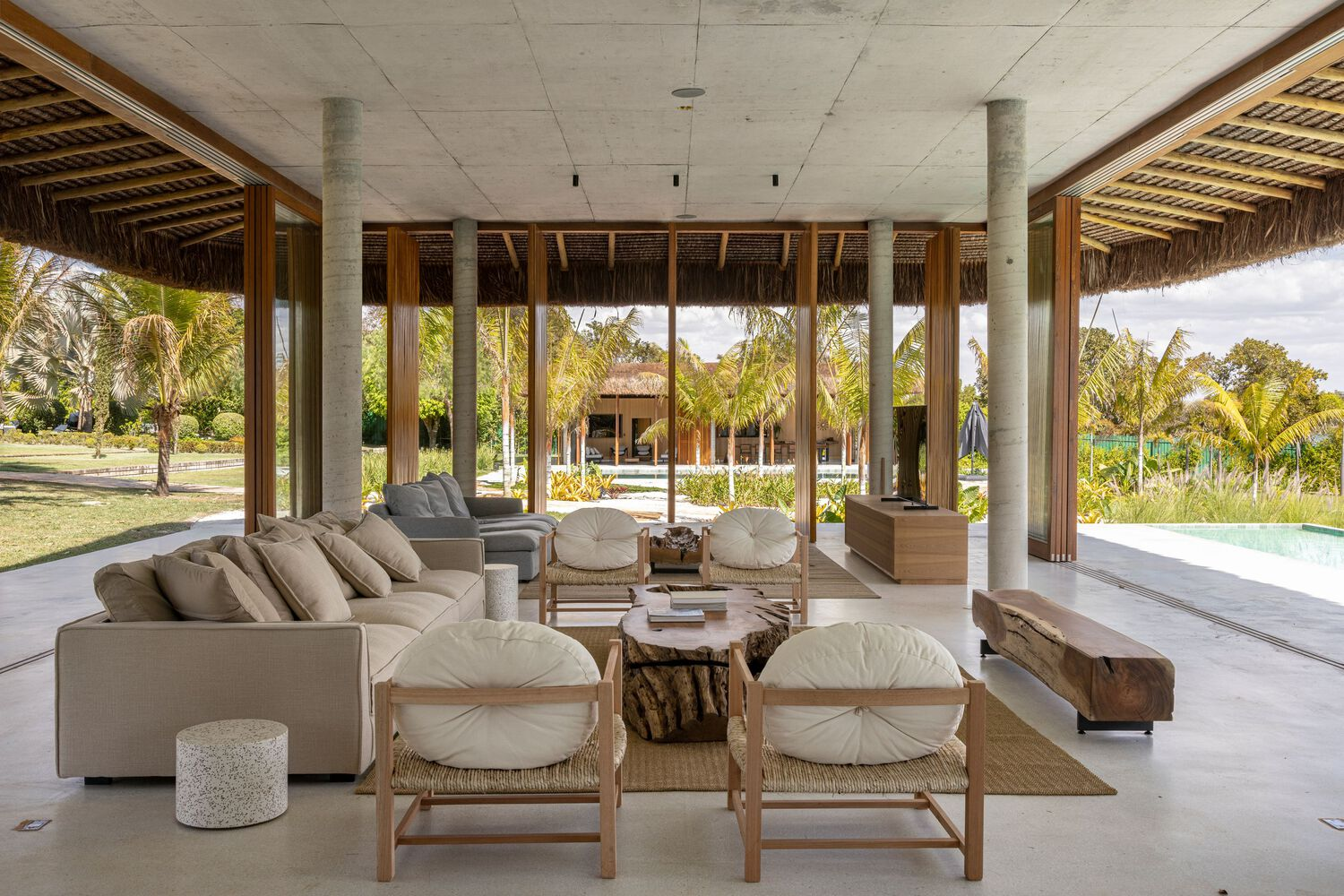 Living area beneath exposed concrete slab ceiling with cylindrical columns framing views to garden