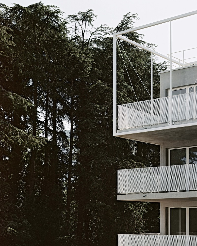 Close-up of cantilevered balconies with perforated metal railings and white tension cables against dense foliage